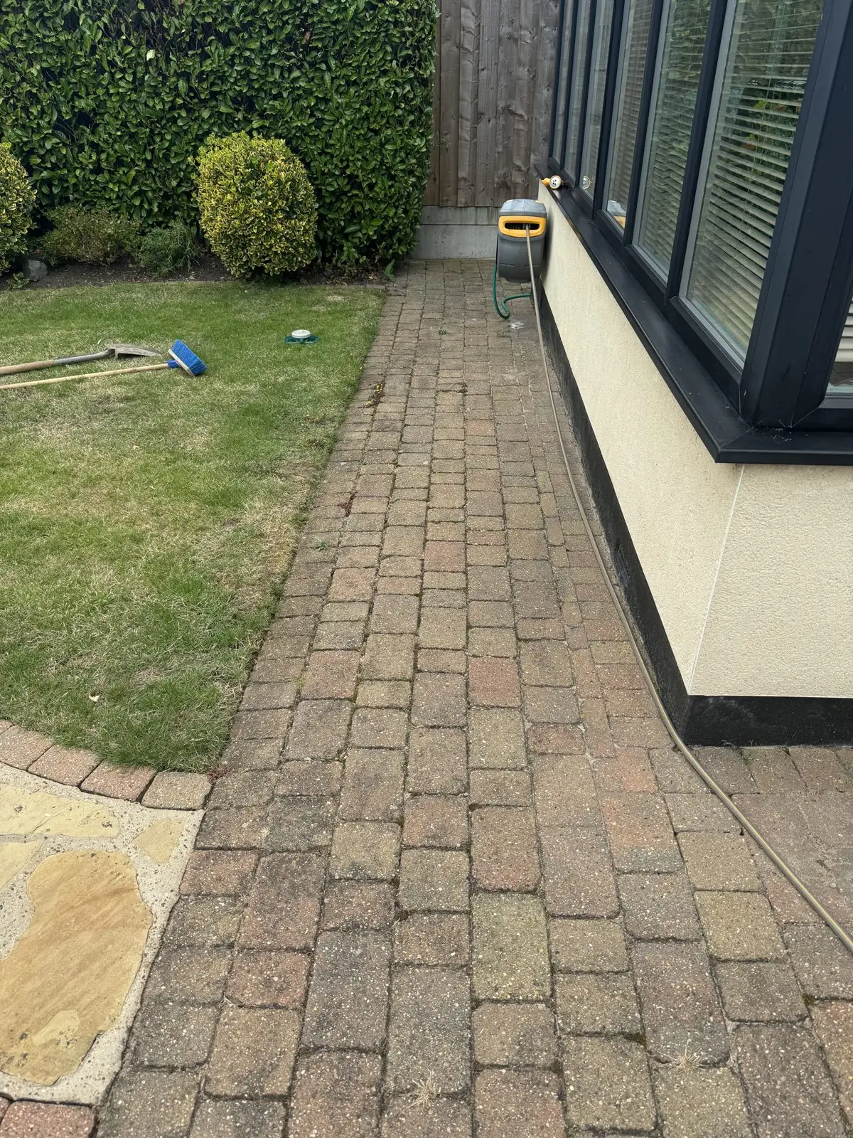 Block paving path beside a conservatory before cleaning, green with algae