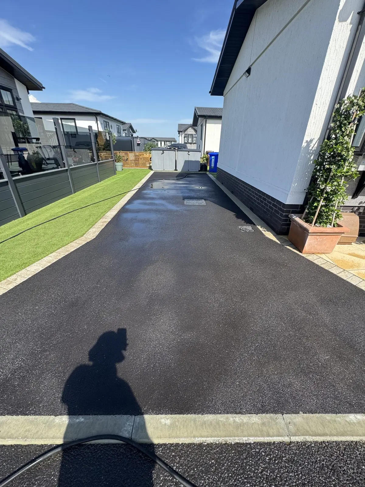 The same tarmac driveway after cleaning, restored to a deep black wet gloss